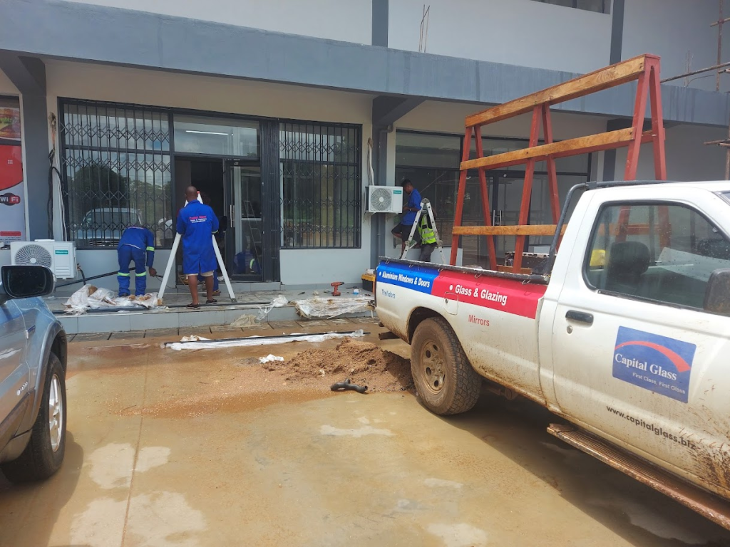 A photo depicting men capital glass staff working and a logo branded car parked aside.